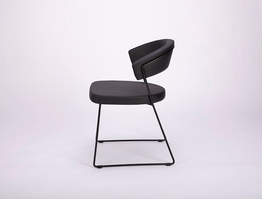 A black leather New York Dining Chair with metal frame and sled base and curved back. Side view.